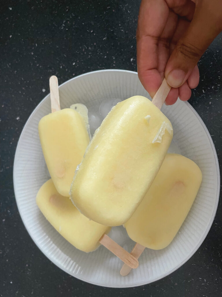 3 popsicles on a white plate with a hand holding a popsicle in front of the plate