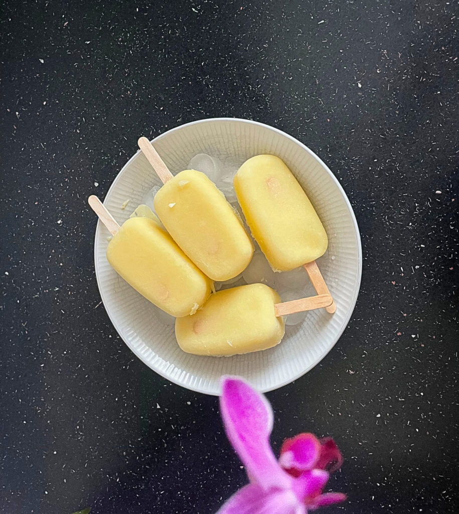 white plate with 4 pineapple sorbet popsicles on a black countertop