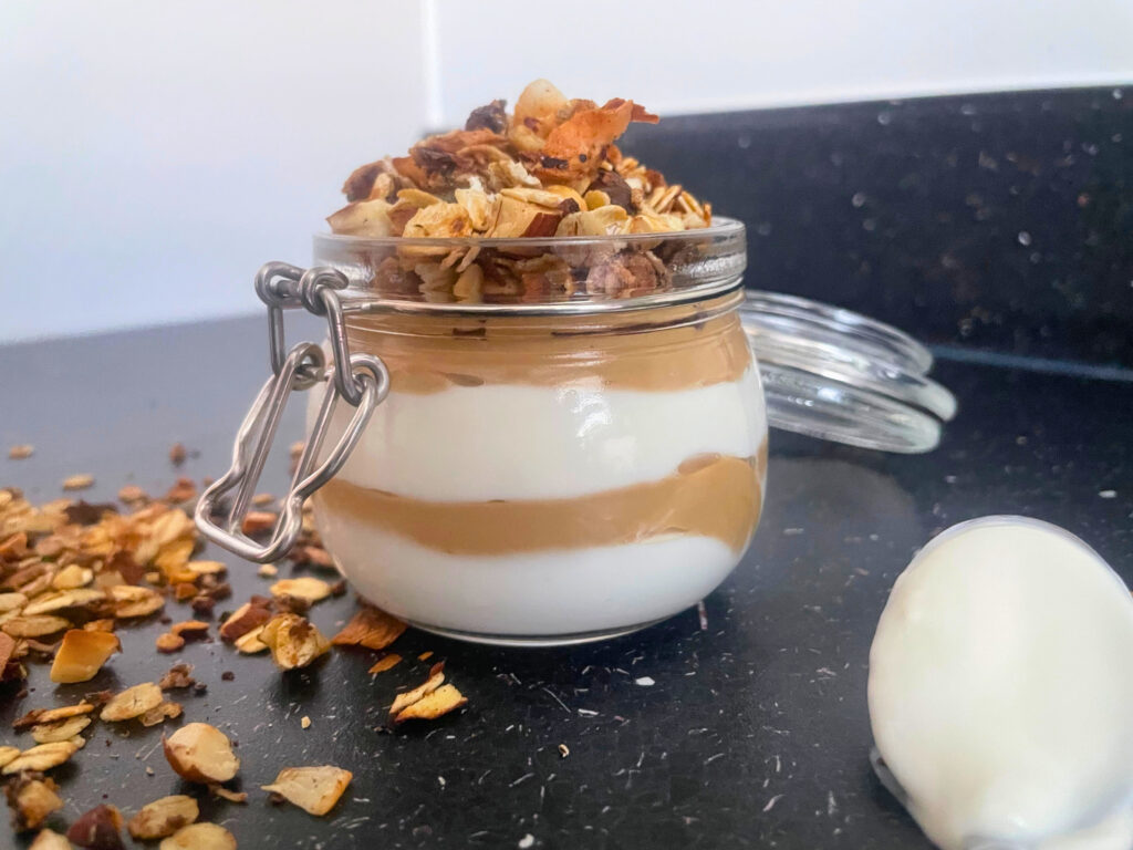 Coconut sugar cream cheese yogurt pot with homemade stovetop granola and a spoon with yogurt on the counter close up