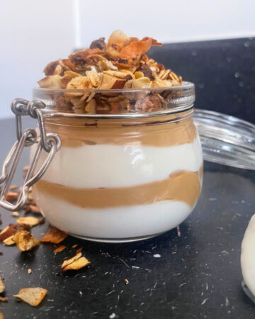 Coconut sugar cream cheese yogurt pot with homemade stovetop granola and a spoon with yogurt on the counter close up