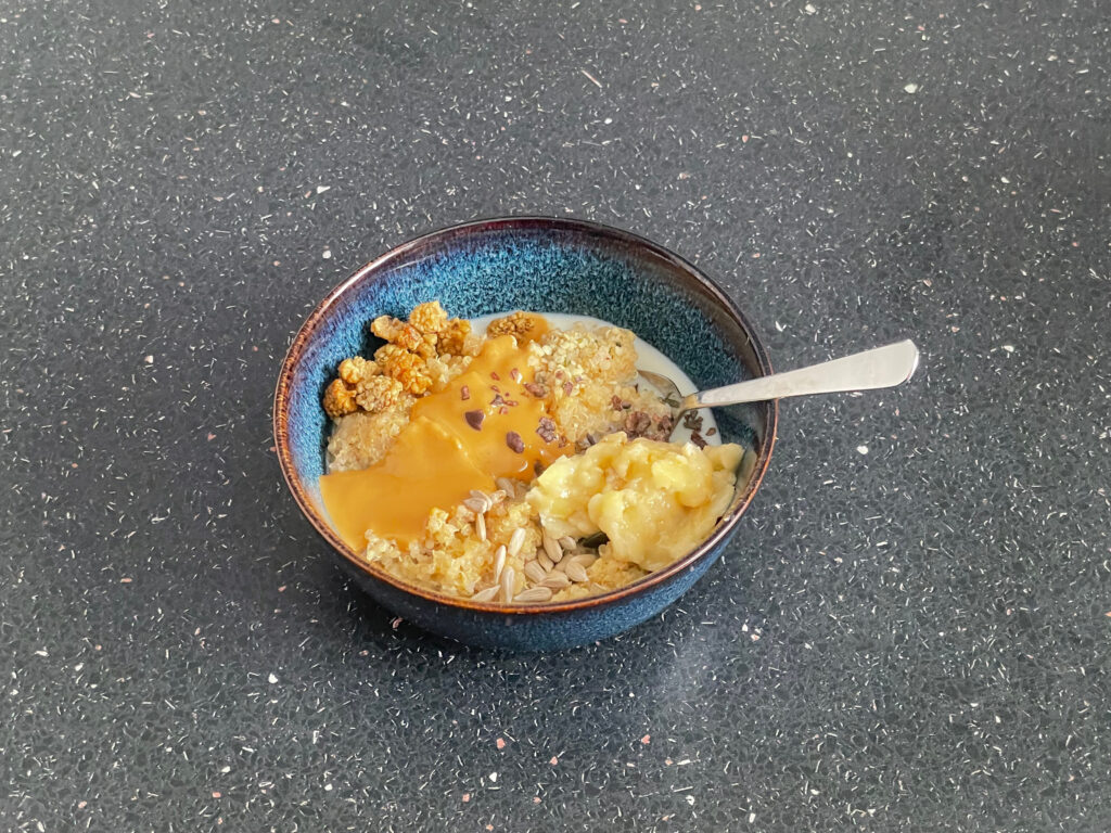 Quinoa breakfast porridge and optional  additions with a spoon in bowl that is on a black counter