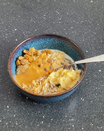 Dressed quinoa bowl with spoon in bowl on a black counter