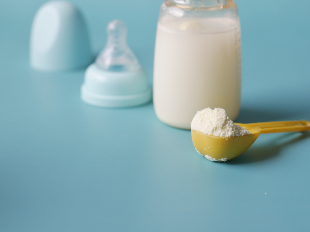 Powdered formula with a bottle in the background that has milk being prepared in it