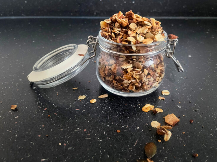 Stovetop granola in a glass pot with a lid on a black countertop