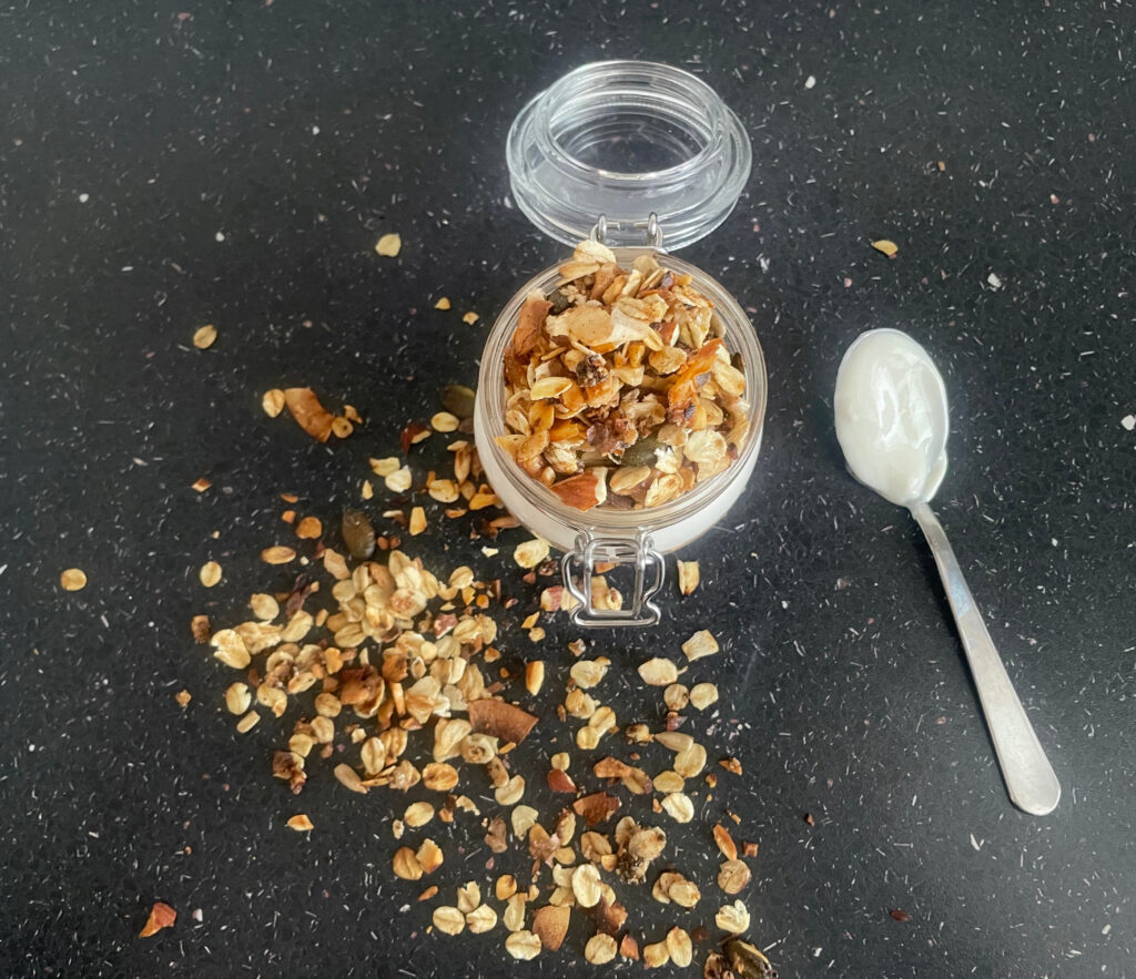 Stovetop granola served with yogurt in a pot with a lid and a spoon with yogurt on the counter