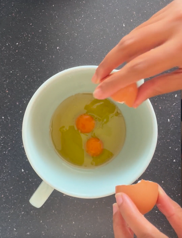 Cracking in two eggs into bowl that has avocado oil