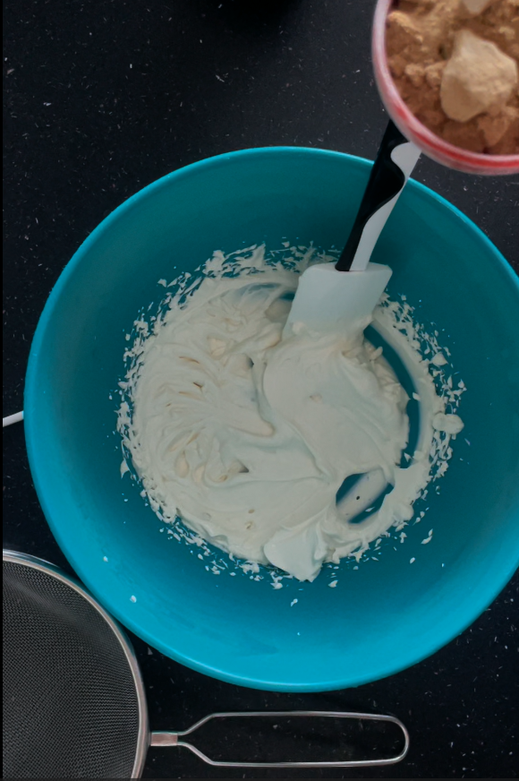 Using a sieve to add in the powdered coconut sugar to the whipped cream cheese 