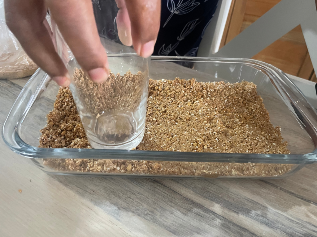 Biscuit base being pressed down in pan with the back of a glass