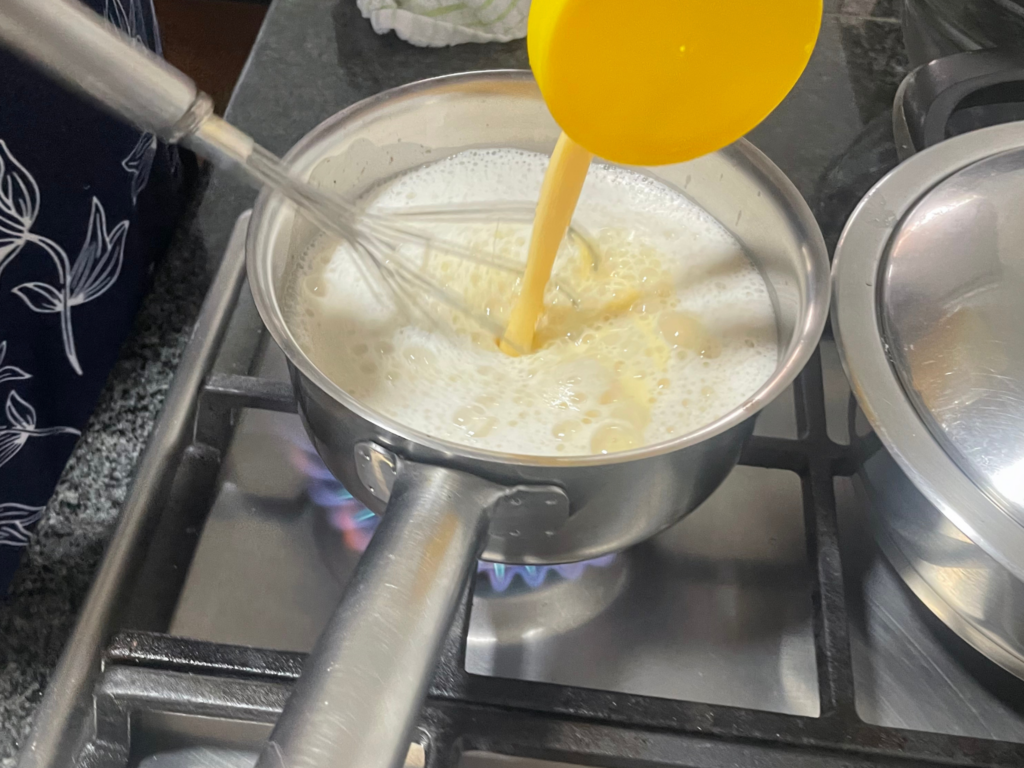 Egg mixture being poured into pot with hot milk and vanilla