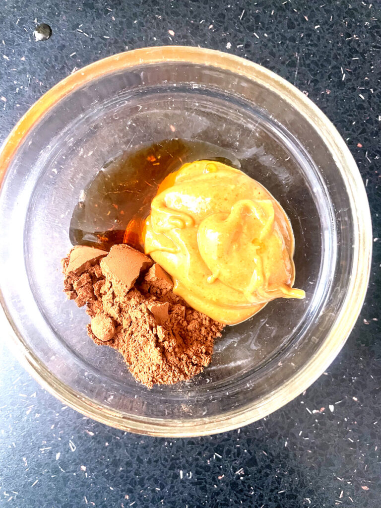 Peanut butter, cocoa powder, and maple syrup in a glass bowl — ingredients for a chocolate peanut butter dip
