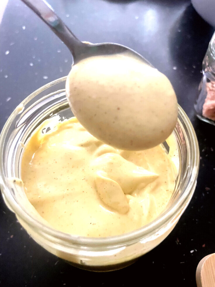 Spoon lifting thick, creamy homemade avocado oil mayonnaise from a glass jar