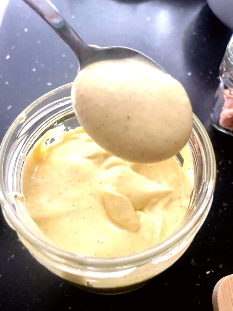 Spoon lifting thick, creamy homemade avocado oil mayonnaise from a glass jar
