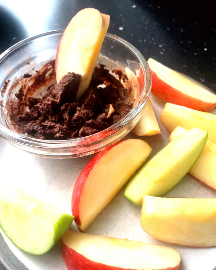Apple slices arranged on a white plate around a glass bowl of chocolate peanut butter dip