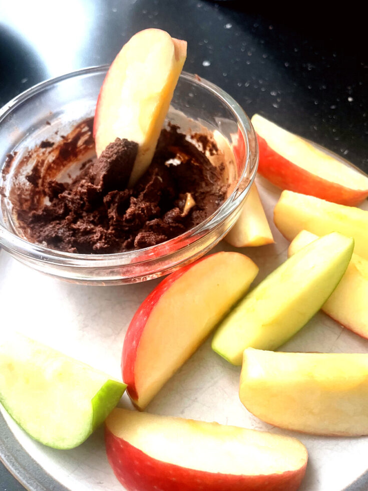 Apple slices arranged on a white plate around a glass bowl of chocolate peanut butter dip