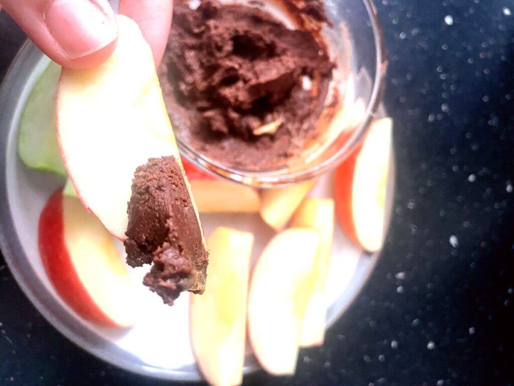 Apple slice dipped in homemade chocolate peanut butter dip held over a plate of apple slices
