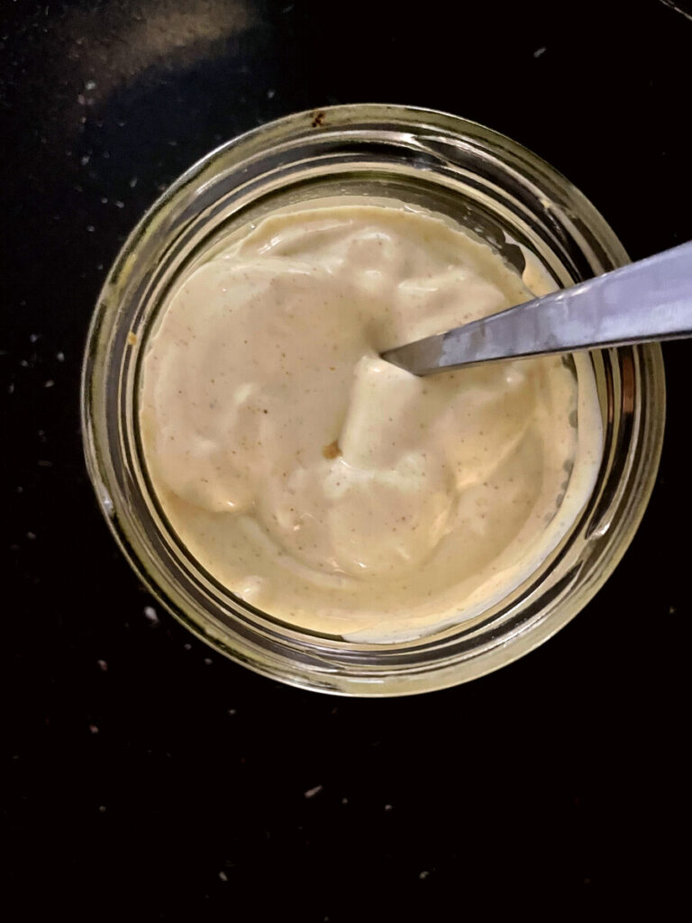 Finished homemade avocado oil mayonnaise in a glass jar, thick and creamy, with a spoon resting inside